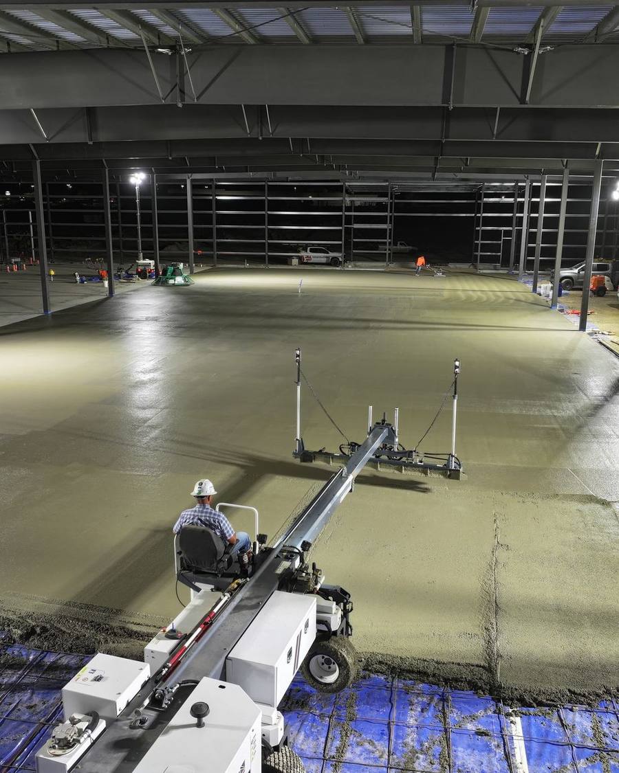Interior of an agricultural steel building with a freshly poured concrete slab being finished